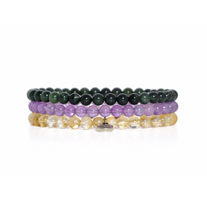 Three beaded stretch bracelets stacked together on a white background. The top bracelet is made of dark green beads, the middle is lavender purple, and the bottom consists of clear faceted beads that appear golden-yellow when highlighted.
