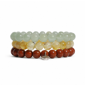 Three stacked beaded bracelets on a white background. The top bracelet features light green translucent beads, the middle features pale yellow translucent beads, and the bottom features dark reddish-brown wooden beads with a small silver metal charm.