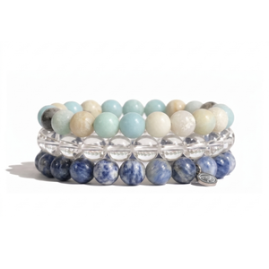 Three stacked beaded stretch bracelets on a white background. The top bracelet features pale mint green and cream beads, the middle is made of clear faceted beads, and the bottom is made of dark blue selenite beads with a small gold-toned metal charm.