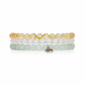 Three beaded stretch bracelets stacked together on a white background. The top bracelet features translucent golden-yellow beads, the middle is clear, and the bottom is light mint green with a small silver-toned oval charm.