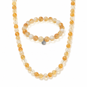 A beaded necklace and matching beaded bracelet set on a white background. The beads are translucent warm amber-orange with some milky white beads, and the bracelet has a small round silver-toned charm.