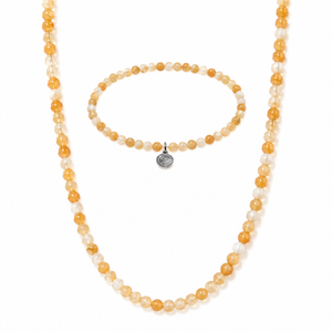A beaded necklace and matching bracelet set on a white background. The beads are faceted in warm amber orange and translucent milky white, with a small round silver-toned charm on the bracelet.