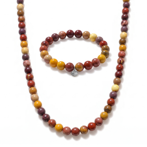 A matching beaded necklace and bracelet set on a white background. The set features round beads in earthy tones of terracotta red, mustard yellow, ochre orange, and brown, with a small silver-toned charm on the bracelet.